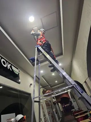 Técnico en una escalera instalando equipo en el techo de un local