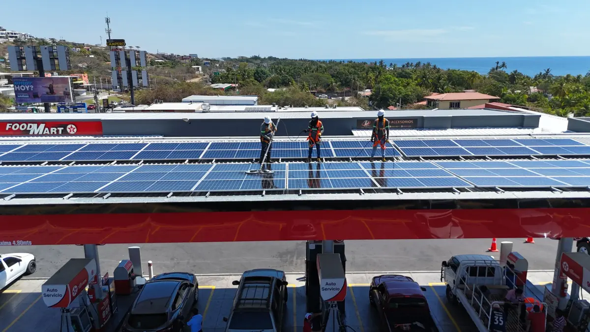 Cuadrilla limpiando paneles solares sobre la canopia de una estación de servicio